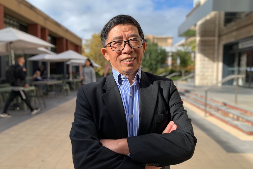 Asian man with black glasses smiling with arms crossed wearing a suit 