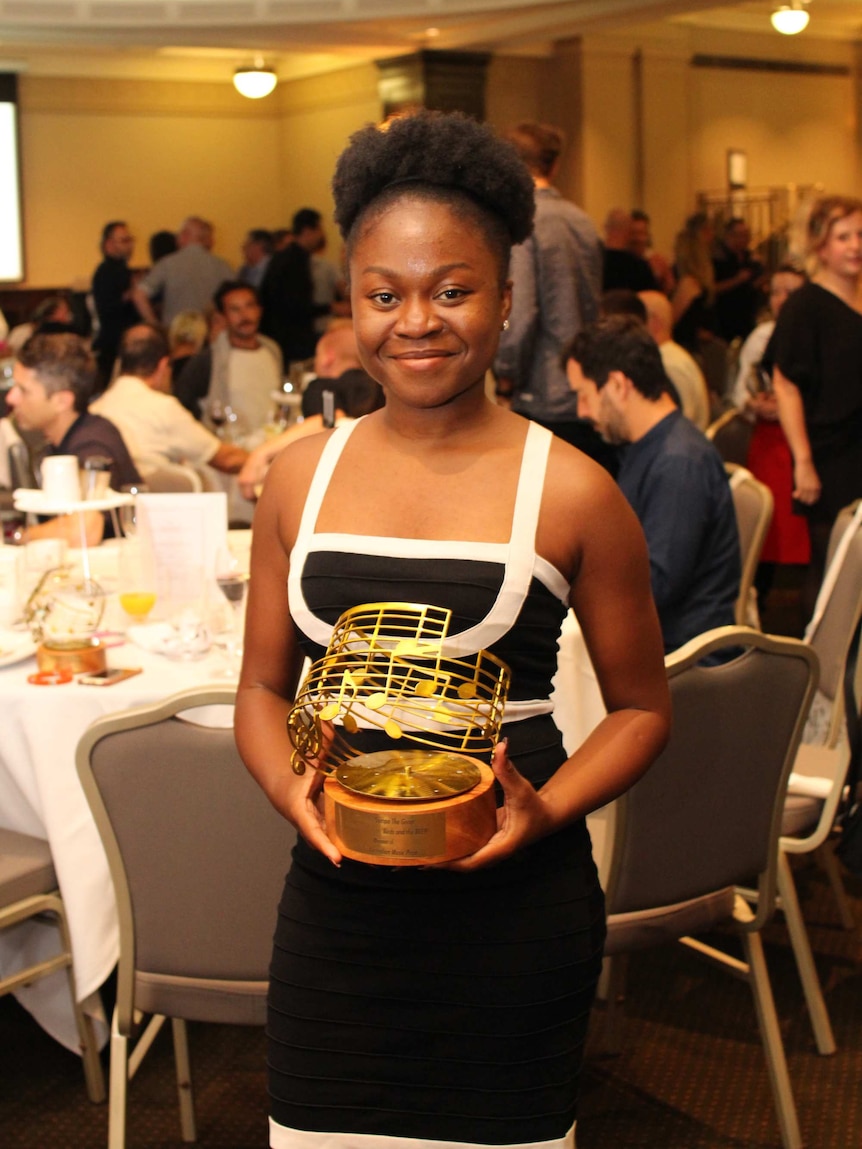 Sampa Tembo stands in a function room, smiling and holding a large gold trophy