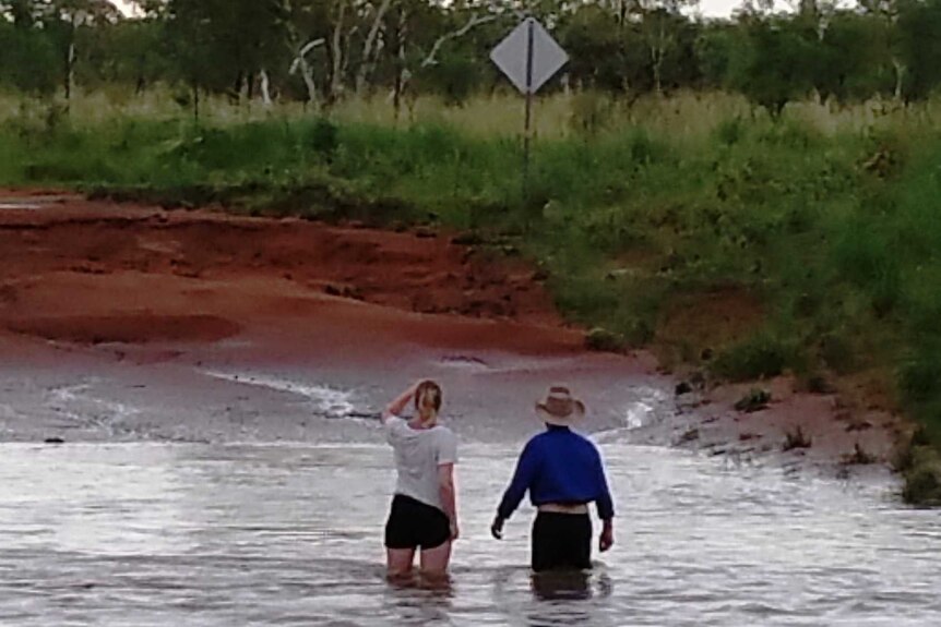 Mid range picture of a man and women wading thigh deep in a flooded section of a red dirt road