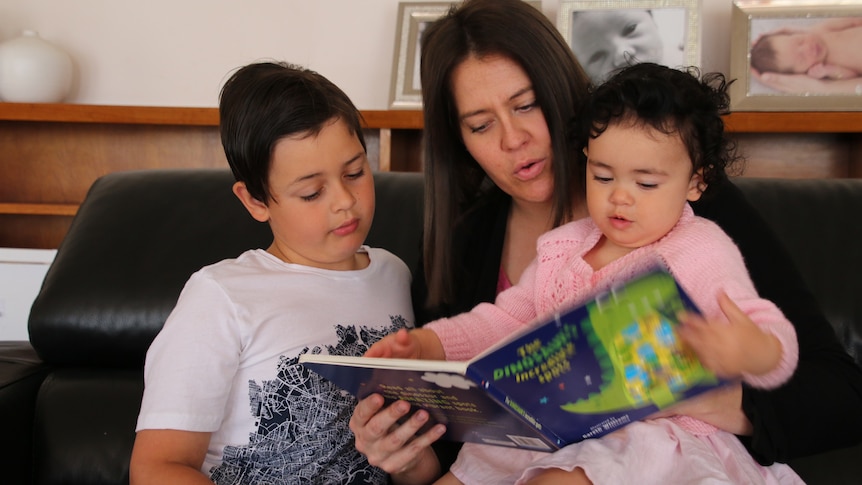 a woman is seen reading to a little by to her left and a little girl to her right