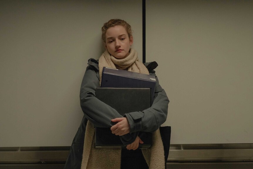 The actor Julia Garner in a scene from the film The Assistant as a downtrodden assistant, laden with folders, in a lift