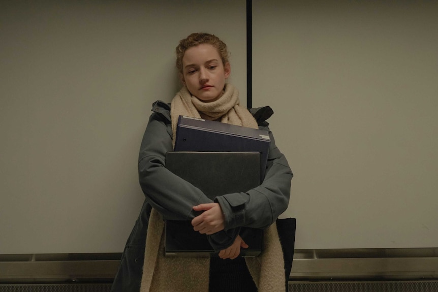 The actor Julia Garner in a scene from the film The Assistant as a downtrodden assistant, laden with folders, in a lift