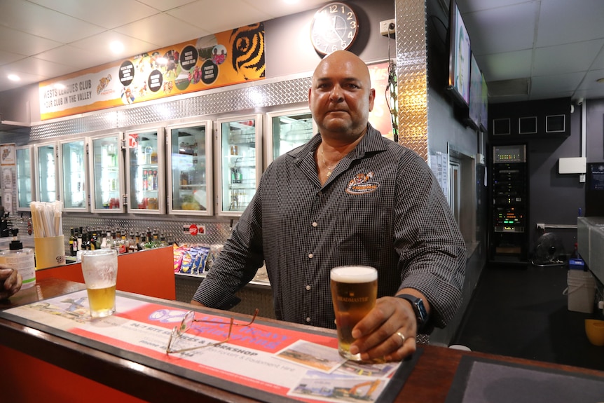 A bartender stands holding a beer.