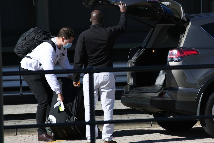 A returned traveller from Melbourne packs his suitcase in a taxi at Perth Airport on the way to quarantine.