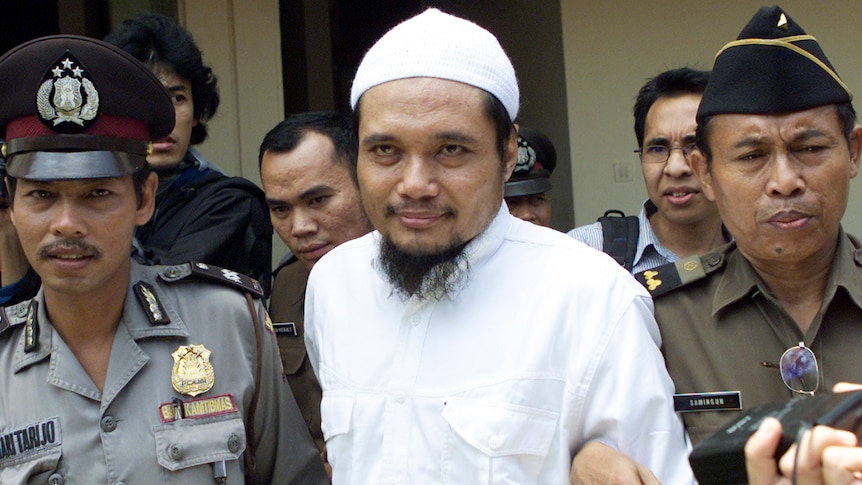 Militant cleric of Jamaah Islamiyah is escorted by security officers after a trial in this 2003 photo.