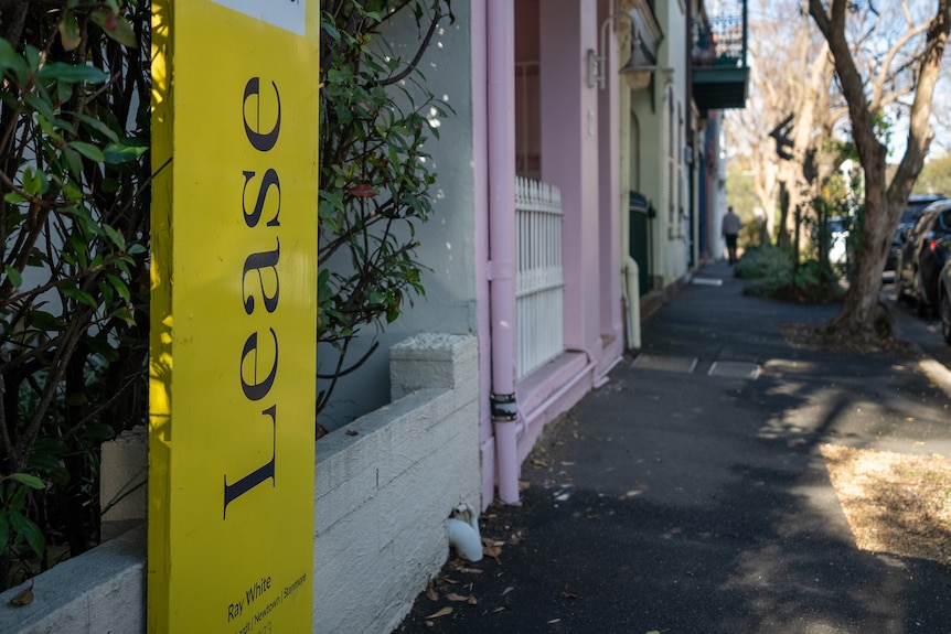 A yellow lease sign outside a row of terrace houses.