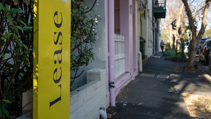 A yellow lease sign outside a row of terrace houses.