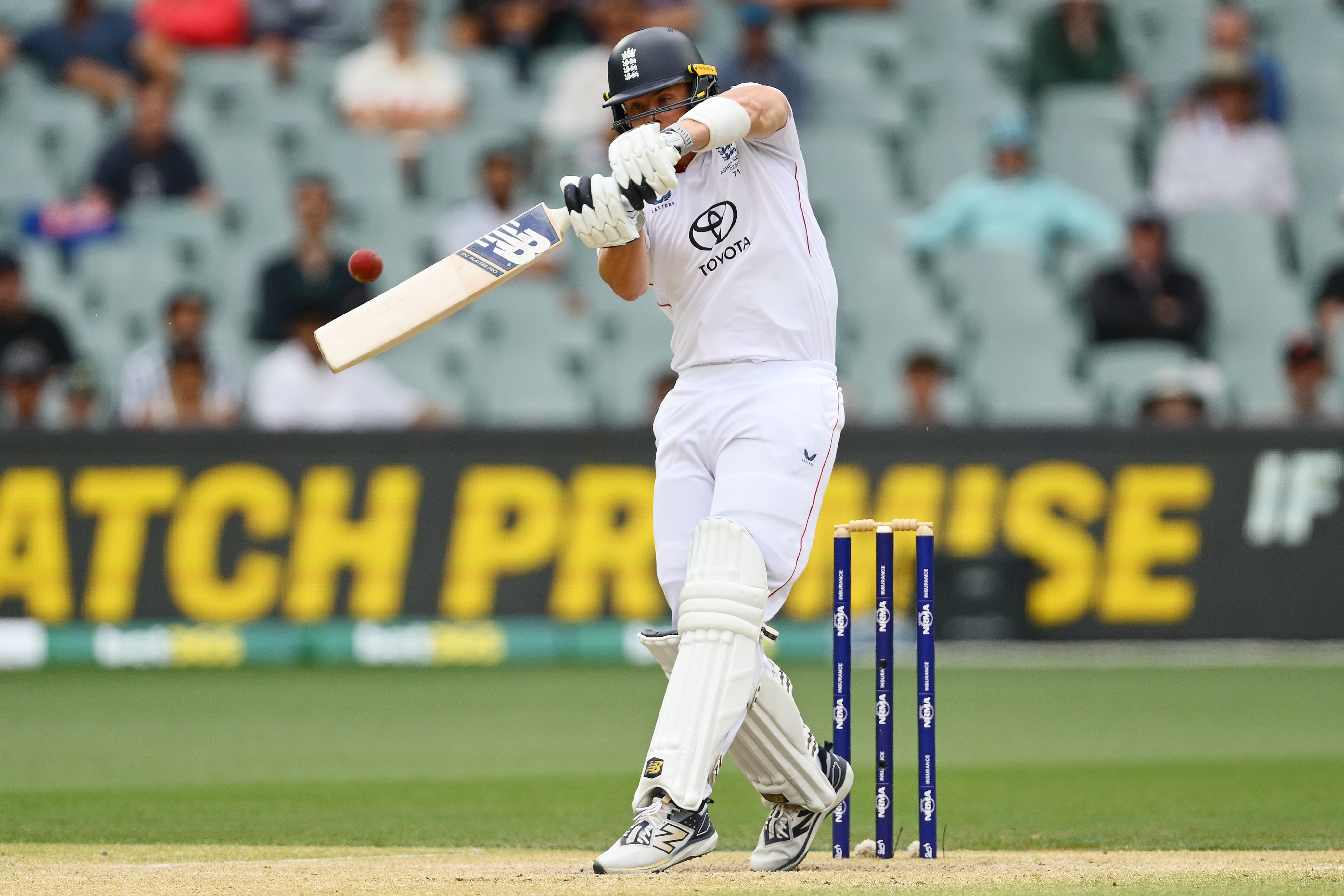 Un bate de críquet dispara a una bola roja delante de sus muñones.