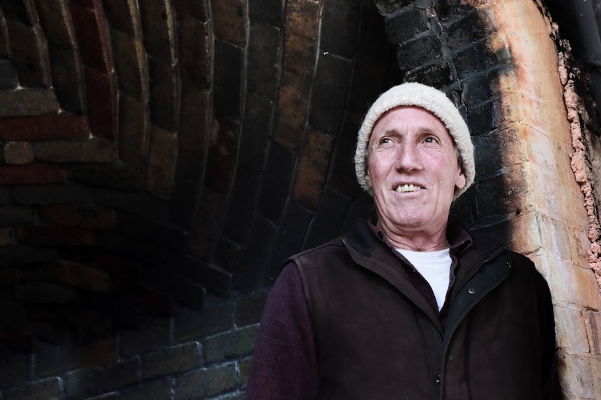 Portrait of man in beanie leaning against the doorway of a brick kiln.