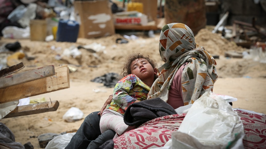 A child rests in her mother's arms while surrounded by debris and garbage.