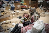 A child rests in her mother's arms while surrounded by debris and garbage.