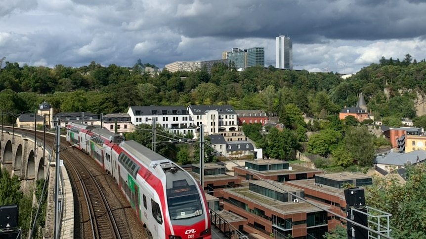 A train on a bridge driving past apartments with larger city buildings in the background. 