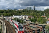 A train on a bridge driving past apartments with larger city buildings in the background. 