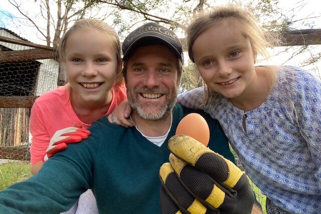 Tom Godfrey holding a fresh laid chicken egg with daughters Poppy, age 11, and Jemima, age 9.
