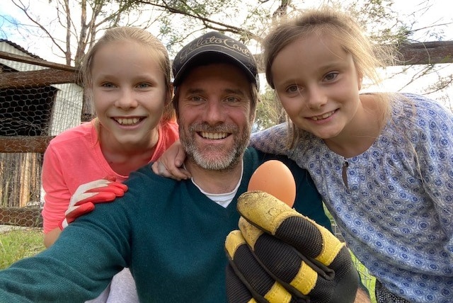 Tom Godfrey holding a fresh laid chicken egg with daughters Poppy, age 11, and Jemima, age 9.