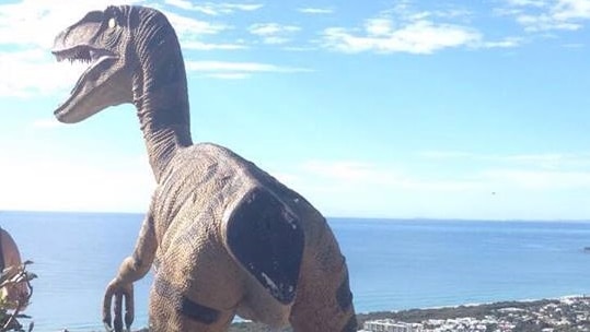 Large dinosaur statue standing on top of a mountain overlooking the ocean