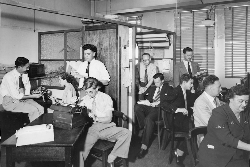People work on typewriters in a 1960s newsroom.