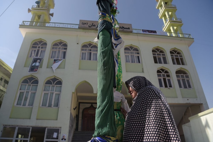 A woman stands at the front of a mosque next to a flagpole