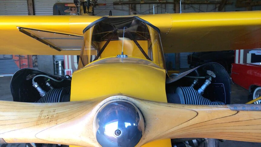 A close up of a planes propeller in the hanger. The plane is yellow and from the 1940s.