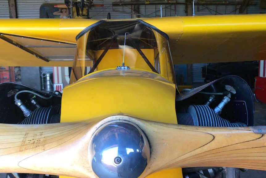 A close up of a planes propeller in the hanger. The plane is yellow and from the 1940s.