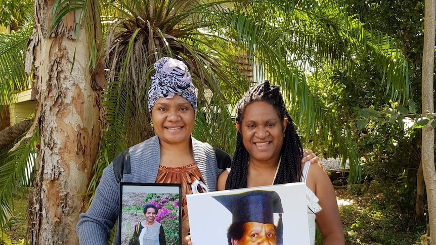 Two women standing side by side, holding a photo of their mother.