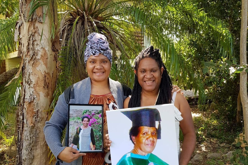 Two women standing side by side, holding a photo of their mother.