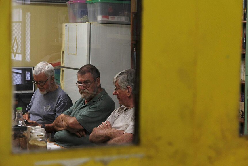 A view through a glass door panel of three elderly gentlemen having coffee and tea.