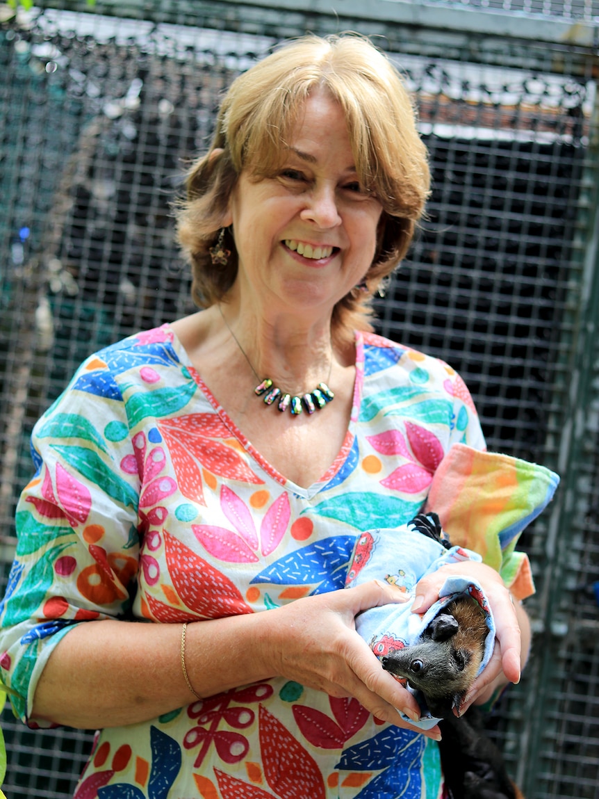 Anne Cherry holds two bats wrapped in cloths outside a bat cage.
