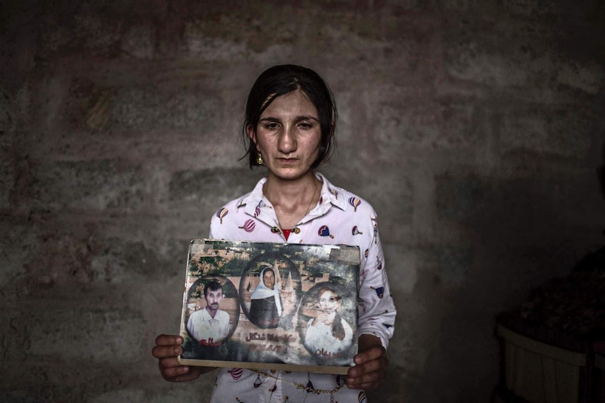 A young woman holds photos of her mother and brother who were killed by Islamic State militants.