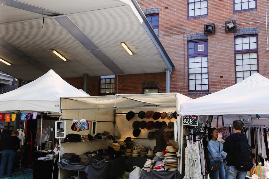 Stalls under white tents selling hats and dresses with red brick buildings behind