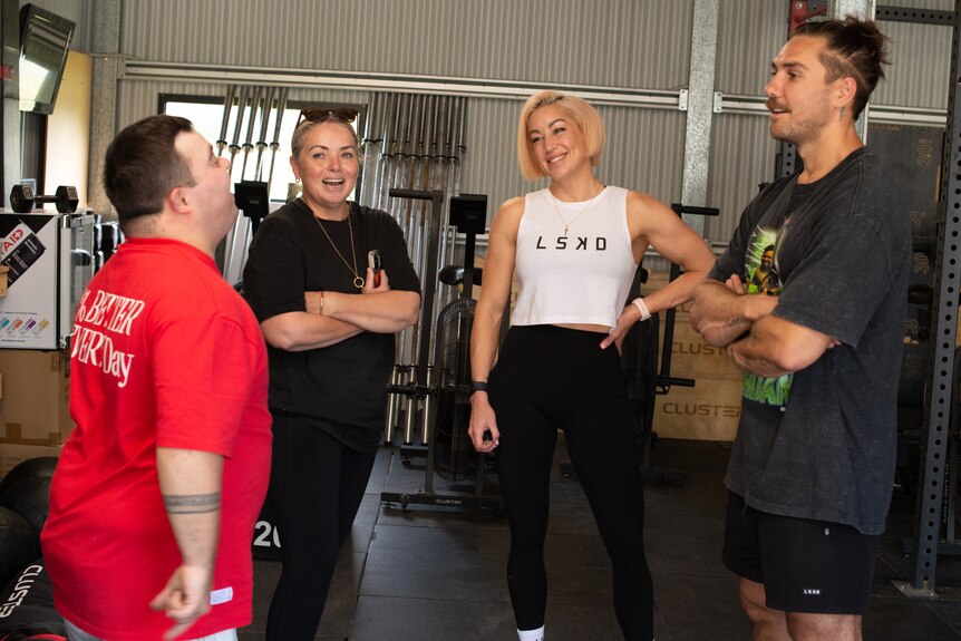 Four people stand in a gym setting, having a conversation.