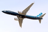 a blue and white Boeing 737 MAX 9 flies in a purplish blue sky