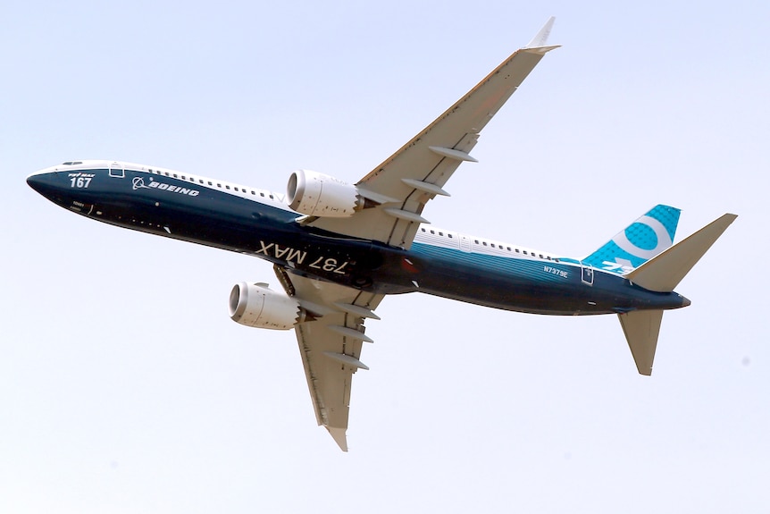 a blue and white Boeing 737 MAX 9 flies in a purplish blue sky