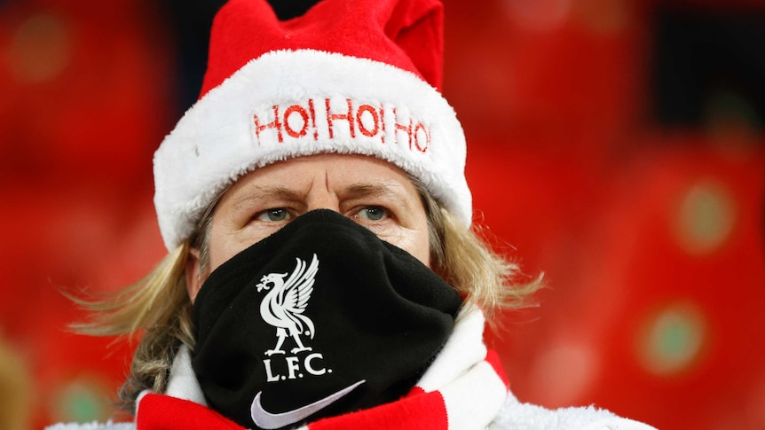 A woman wearing a Liverpool FC face mask and santa hat that says Ho! Ho! Ho! grimaces as she watches football