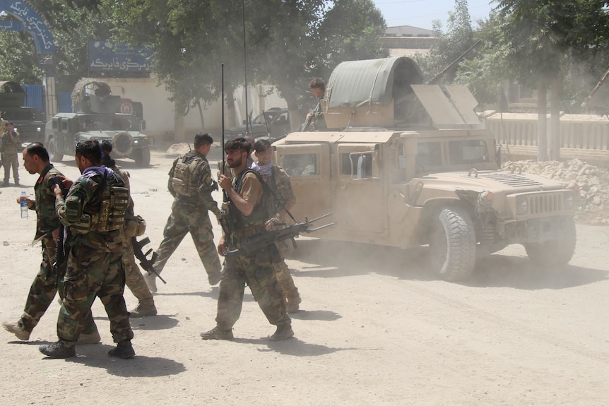 A group of soldiers walk away from a humvee in a dusty street.