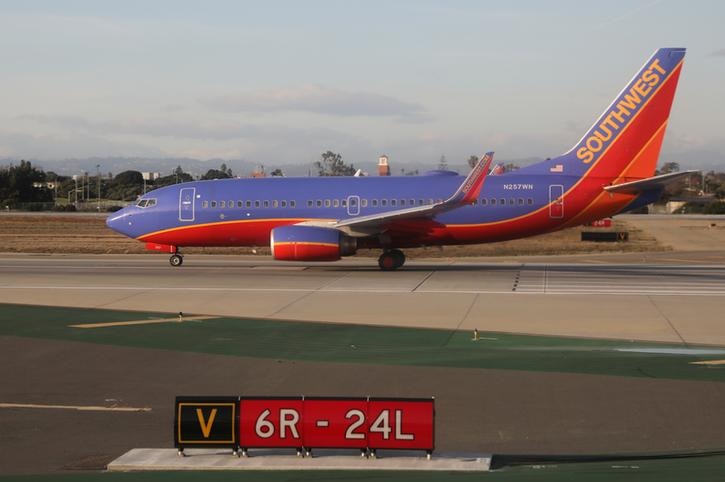 A blue, red and orange Southwest Airline plane sits on the tarmac in the background with blue skies in the backdrop.