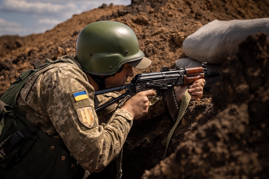 A man wearing a helmet and army fatigues points a gun on the ground.