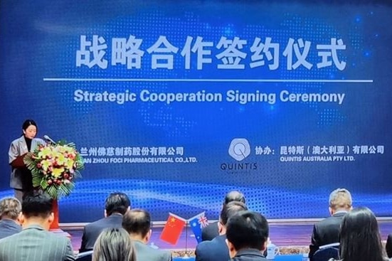 Photo of a signing ceremony in front of blue sign with Chinese writing