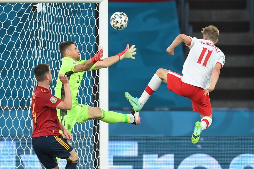 A Polish footballer leaps high and boots the ball over the bar as the goalkeeper tries to spread himself at Euro 2020.