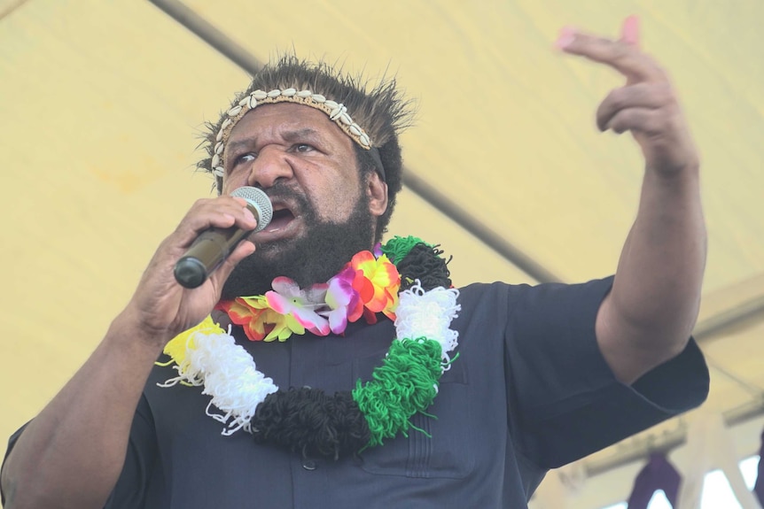 Opposition leader Don Polye talks into a microphone.