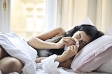 Woman lying on bed while blowing her nose into a tissue 