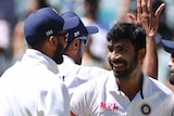 Jasprit Bumrah smiles and looks at his teammate as a group of men crowd around him