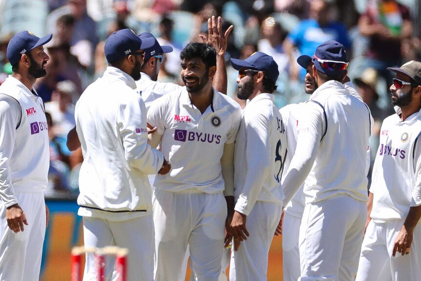 Jasprit Bumrah smiles and looks at his teammate as a group of men crowd around him