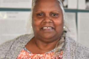 Closely cropped image of an Aboriginal woman wearing a grey cardigan and colourful shirt.