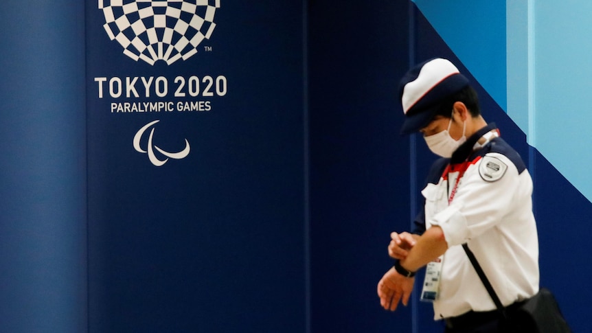 A man checks his watch while standing in front of the Tokyo Paralympics logo.