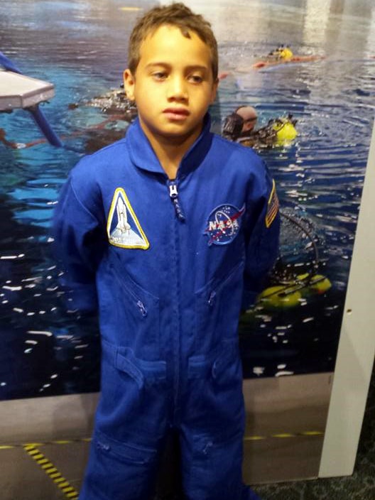 Rua wears a spacesuit and stands in front of a picture of divers.