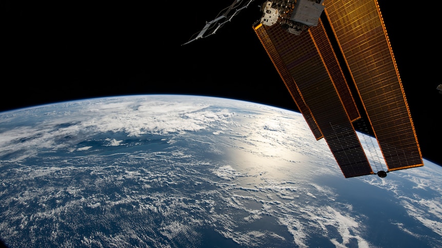 The earth is pictured from Space with a half circle on the horizon with on the right part of the International Space Station
