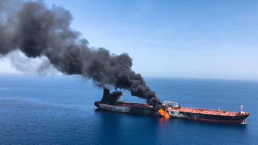 An oil tanker at sea on fire near the Strait of Hormuz, with a large cloud of smoke coming out of it.