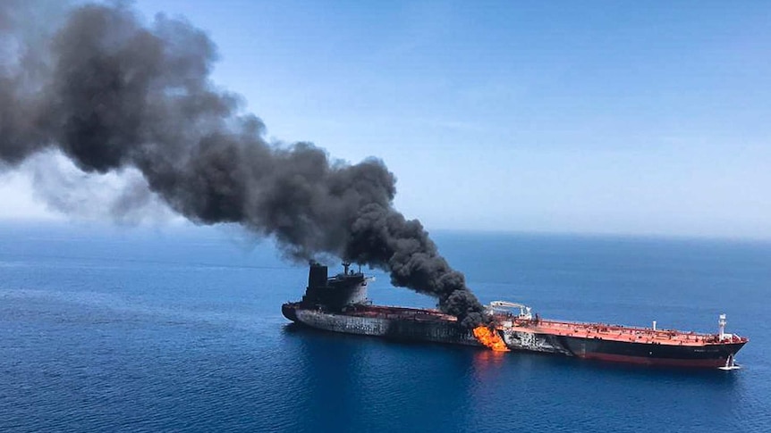 An oil tanker at sea is on fire with a large cloud of smoke coming out of it