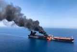An oil tanker at sea on fire near the Strait of Hormuz, with a large cloud of smoke coming out of it.
